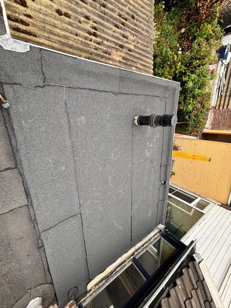 Plat dak met nieuwe bitumen toplaag, afgewerkte dakdoorvoer en witte daktrim in Arnhem