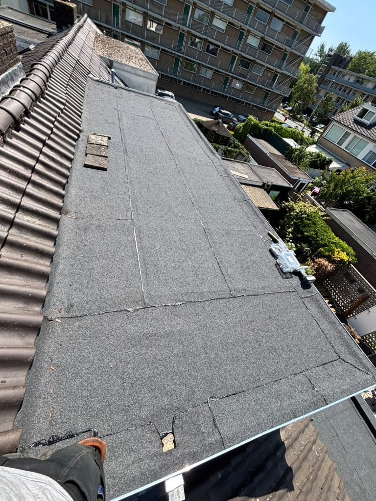 Langgerekt plat dak met nieuwe bitumen toplaag en daktrim tussen twee pannendaken in Arnhem