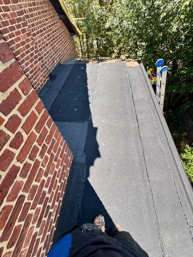 Vernieuwd plat dak met bitumen toplaag, afgewerkte kim en daktrim langs een bakstenen gevel in Eindhoven